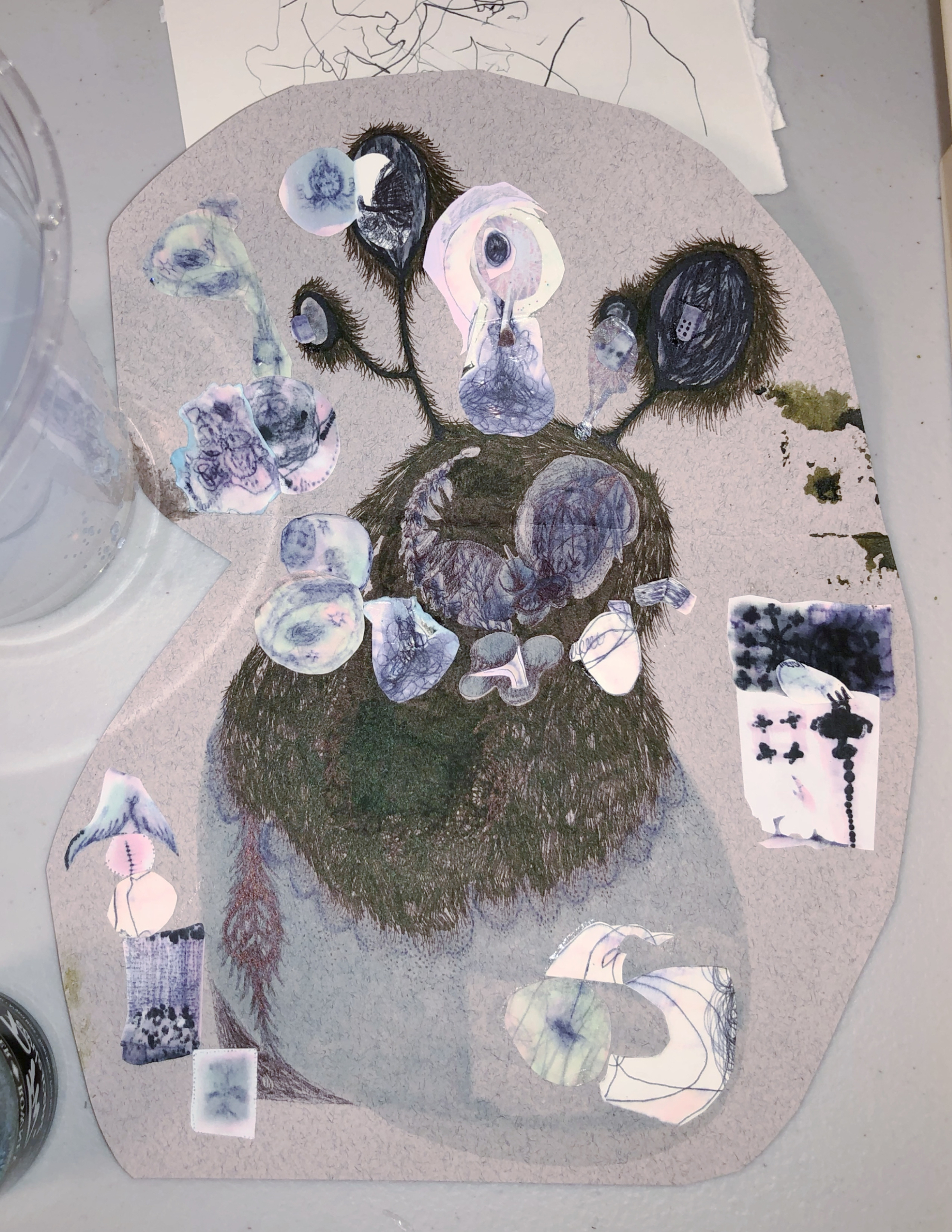 Auto-generated description: A mixed-media artwork features a dark, textured, furry creature with multiple eye stalks surrounded by abstract shapes and cut-out paper elements on a grayish background.